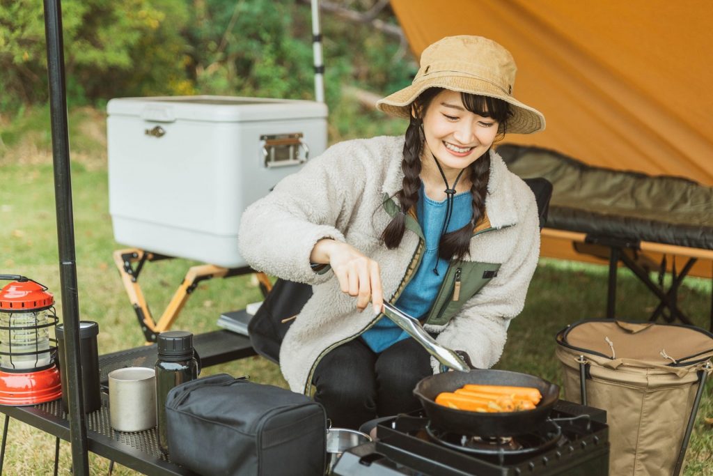 屋外でキャンプ飯・料理を作る若い女性キャンパー